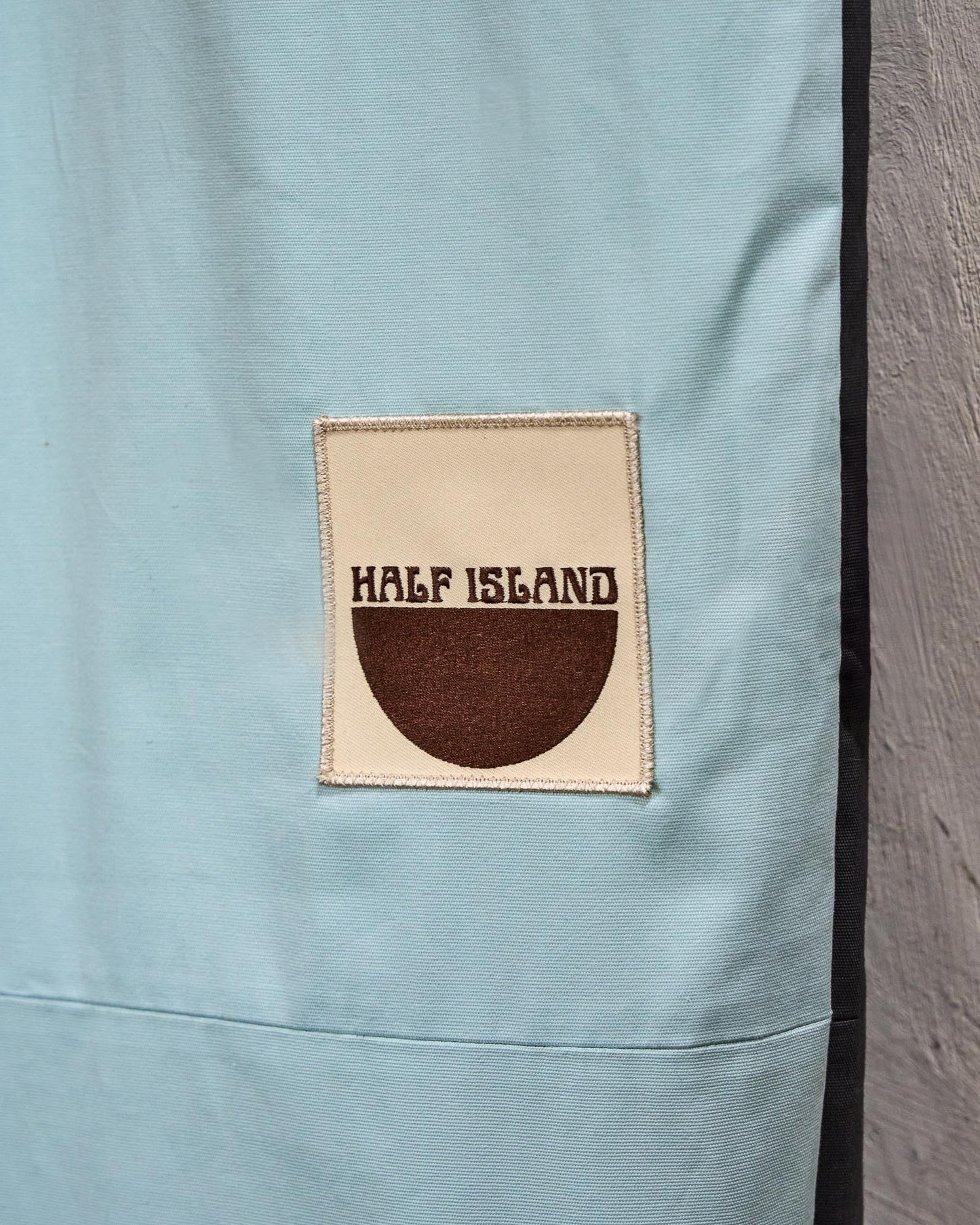 Close-up of a light blue fabric surfboard cover with a 'Half Island' logo patch.