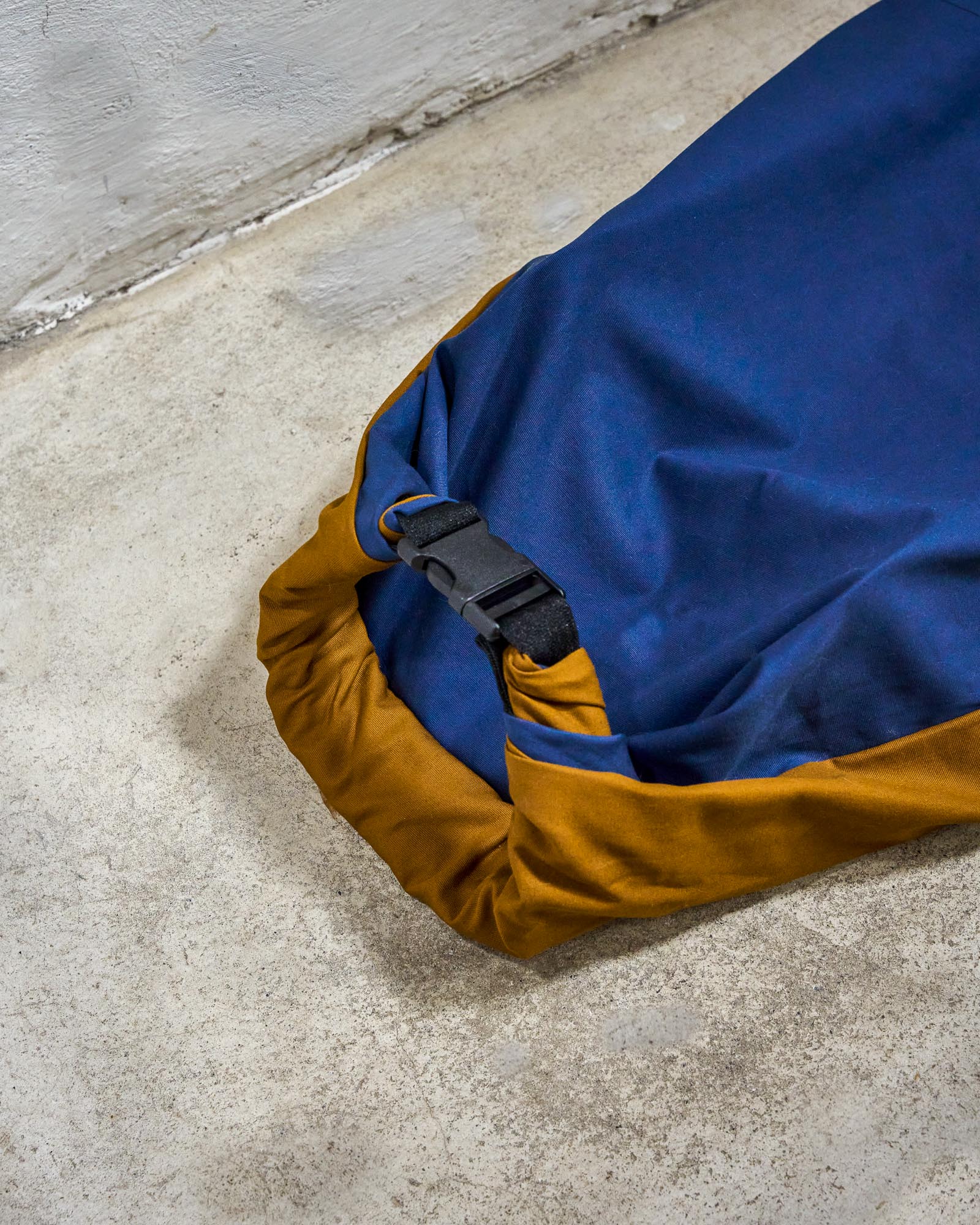 Blue and brown surfboard bag with a black buckle on a concrete surface.