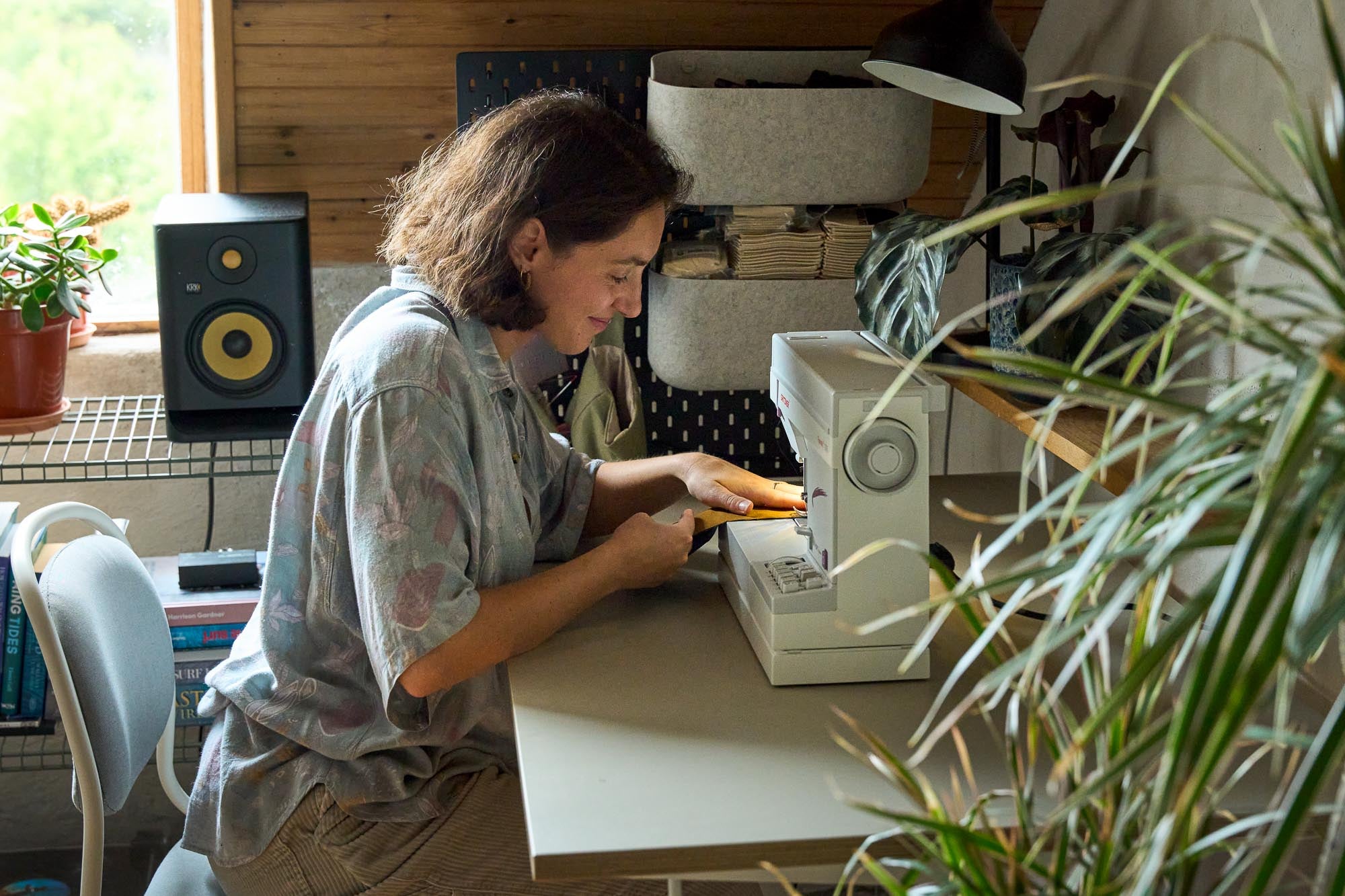 Person using a sewing machine to make handmade surfboard bags in a room with plants.