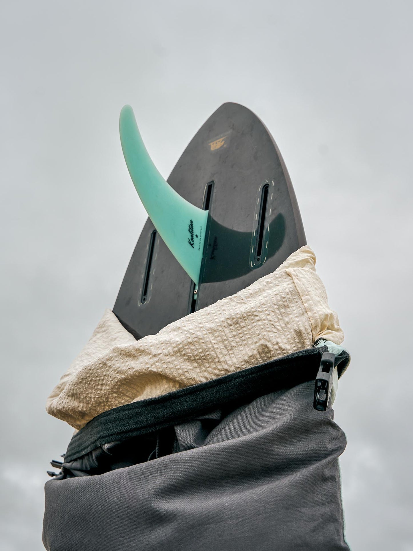 Single fin surfboard in a grey board cover against a cloudy sky.