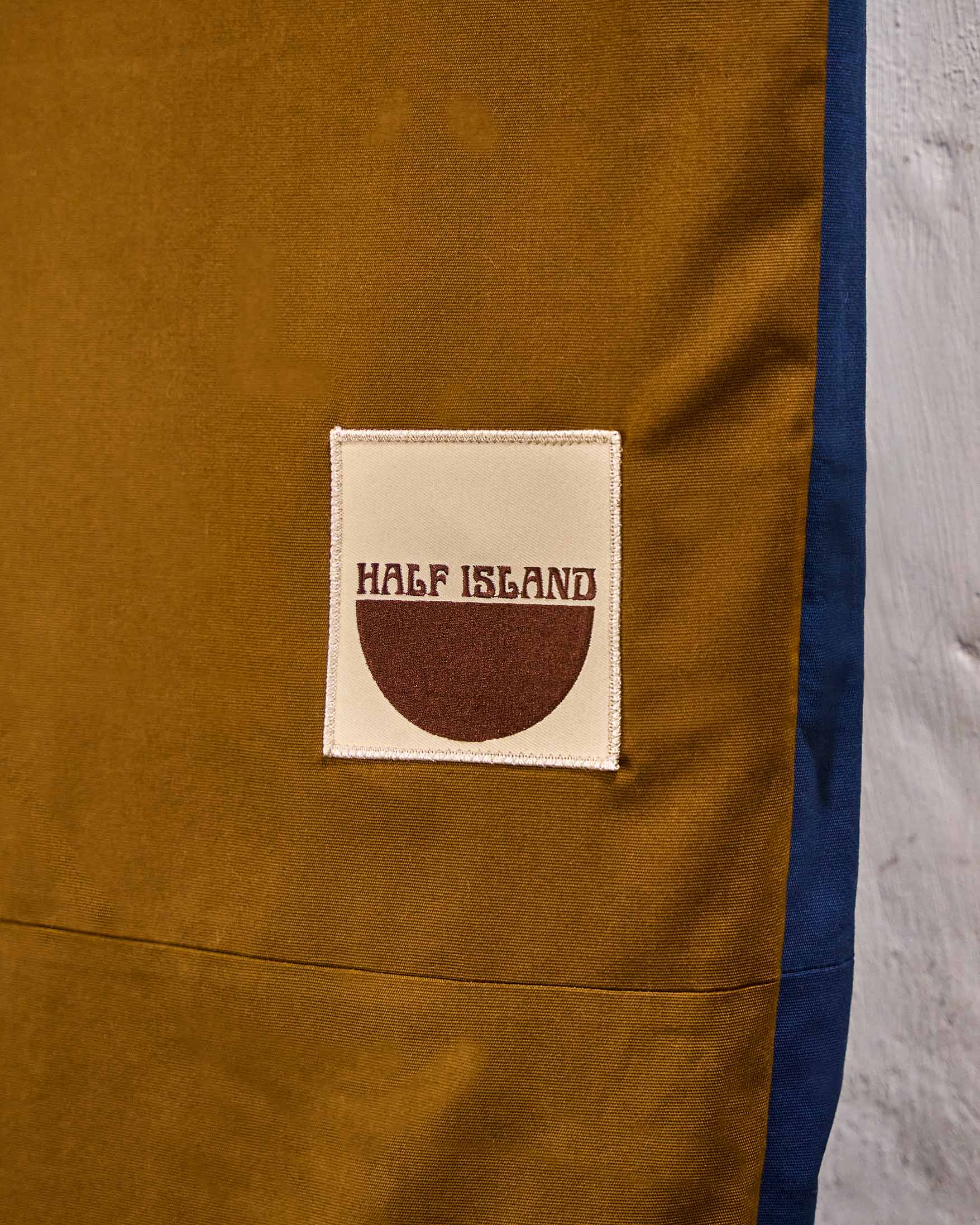 Close-up of a brown surfboard bag with 'Half Island' logo on a gray background.