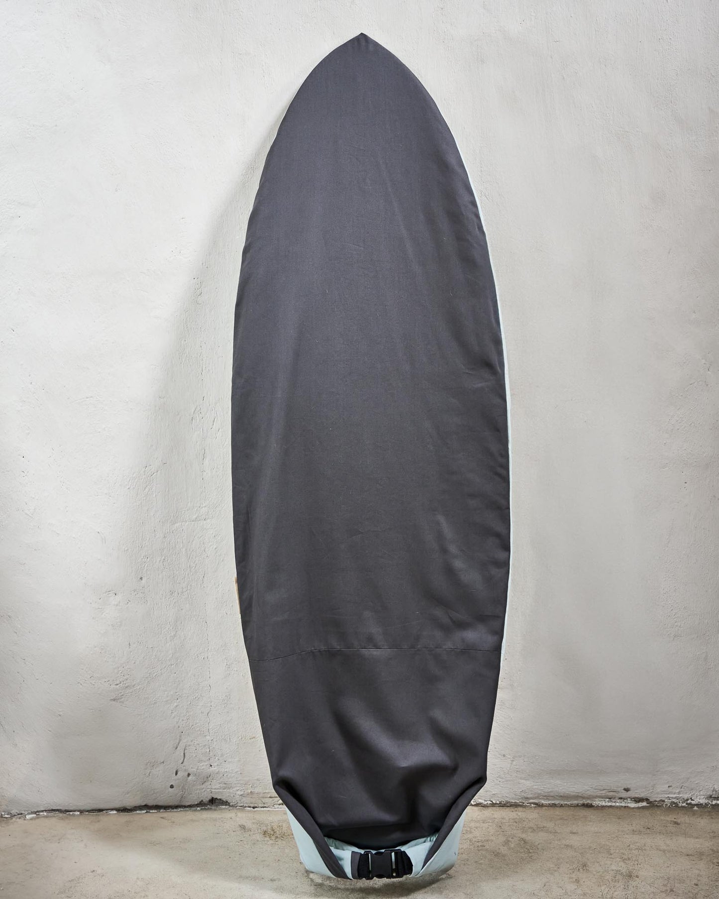 Handmade grey surfboard cover on a fish against a grey wall.