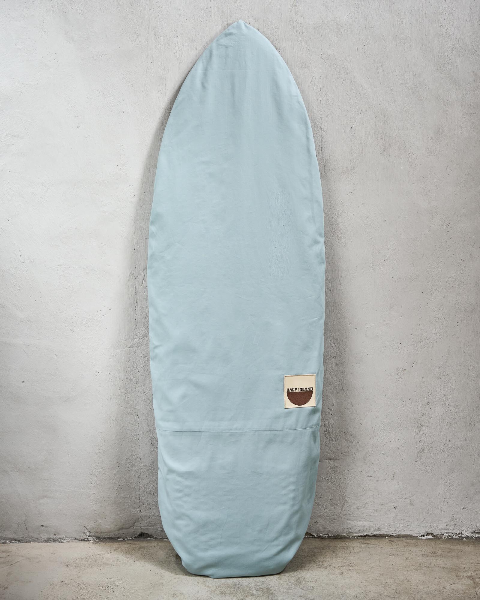 Handmade light blue surfboard bag with a logo against a grey wall.