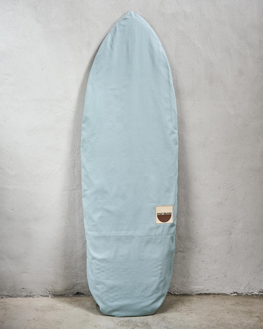 Handmade light blue surfboard bag with a logo against a grey wall.