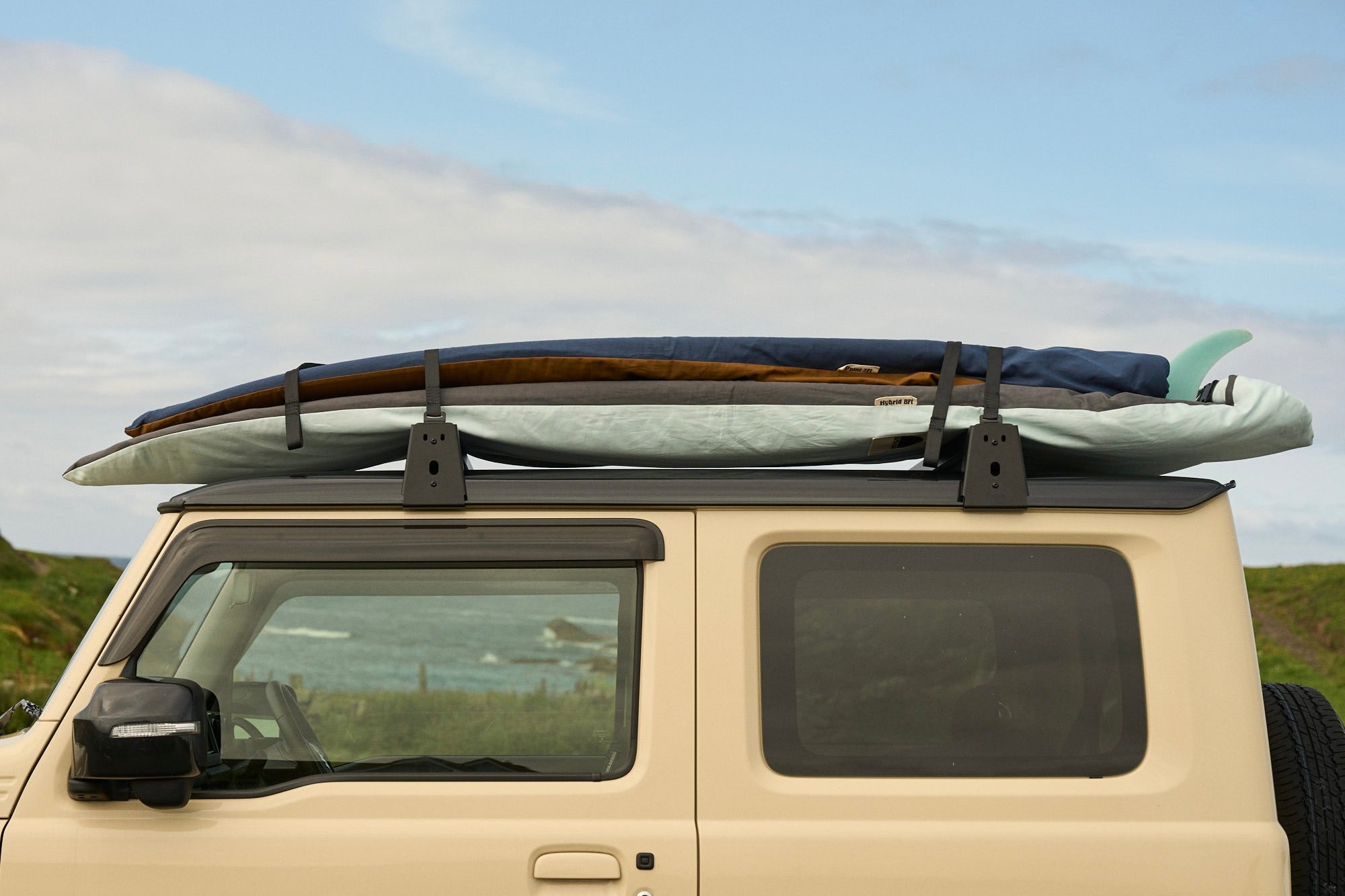 Car with a two surfboards in board covers on the roof against a scenic background.
