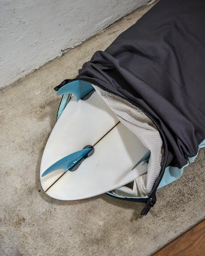 White surfboard with blue fins partially covered by a grey surfboard bag.