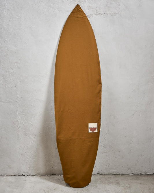 Handmade brown surfboard bag with a logo on a grey wall.