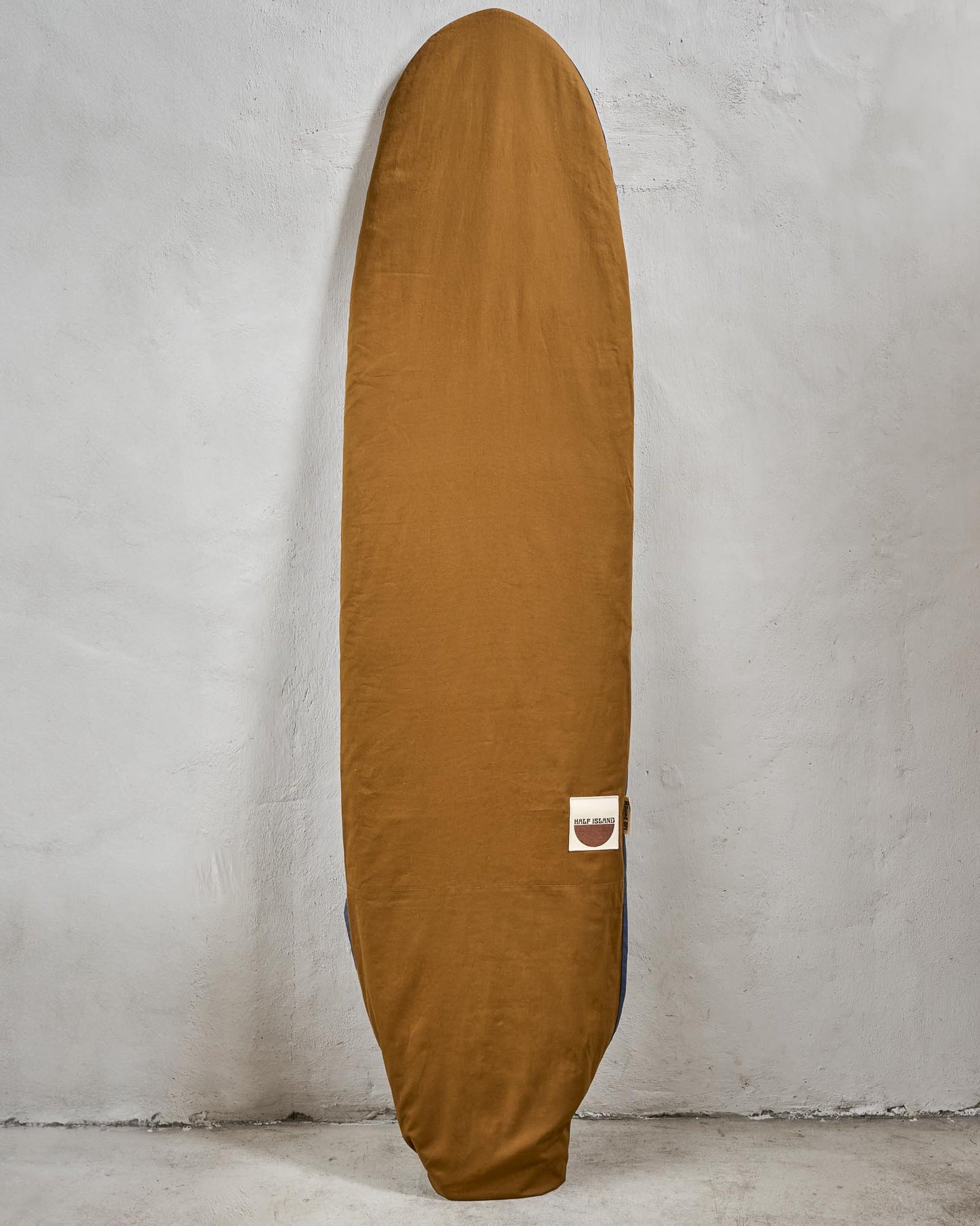 Handmade brown surfboard bag with a logo on a grey background.