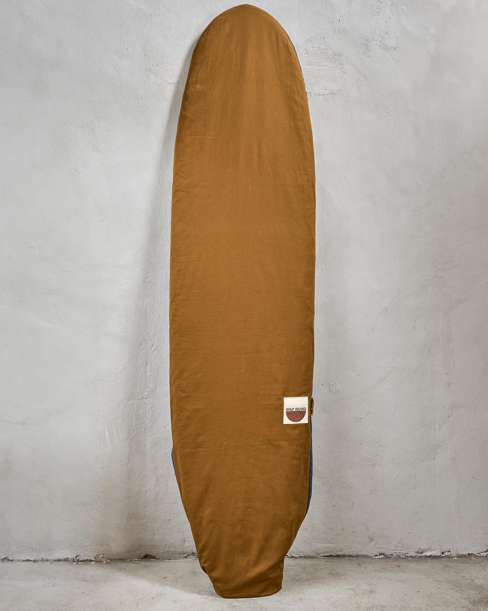 Handmade brown surfboard bag with a logo on a grey background.