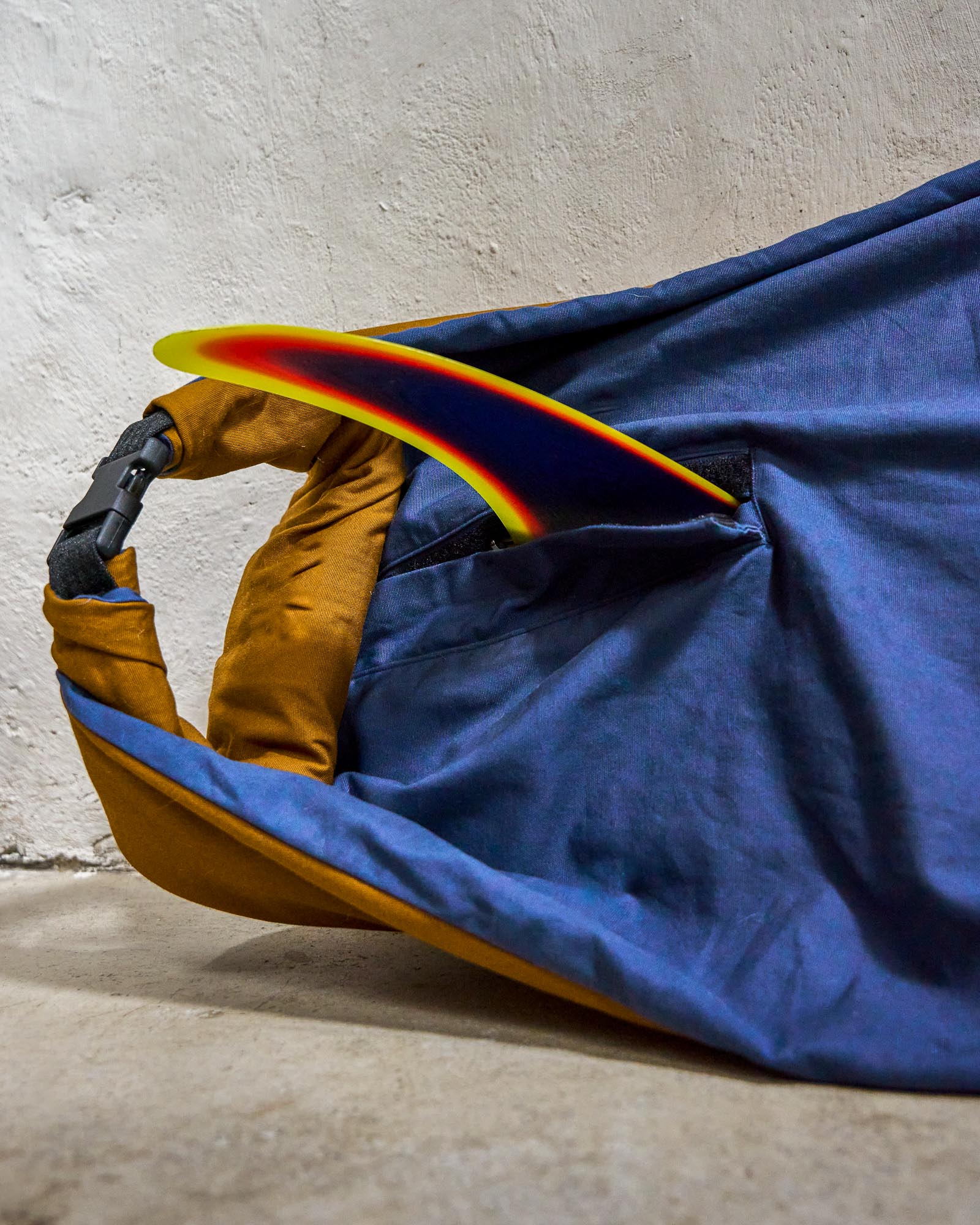 Detail picture showing a single fin slit on a rolled up blue surfboard bag.